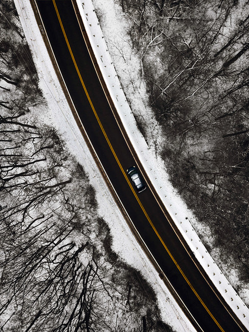 An aerial view of a winding road surrounded by snowy landscapes and trees, with a car driving along the road.